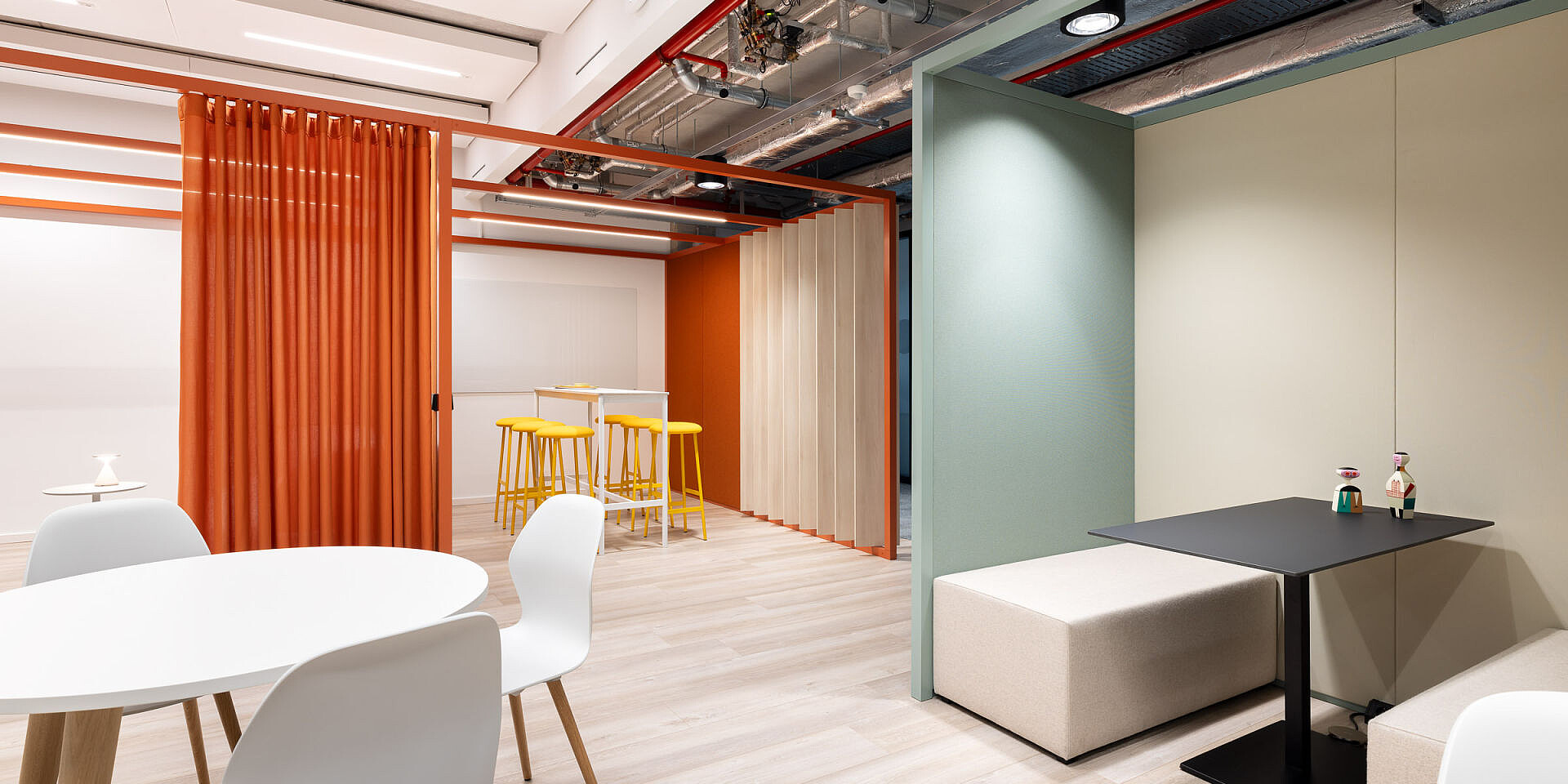 Moderner Bistro-Bereich bei Veolia mit weißen se:spot Designstühlen und schwarzen se:assist Tischen, umgeben von orangen Vorhängen und Holzrahmen.