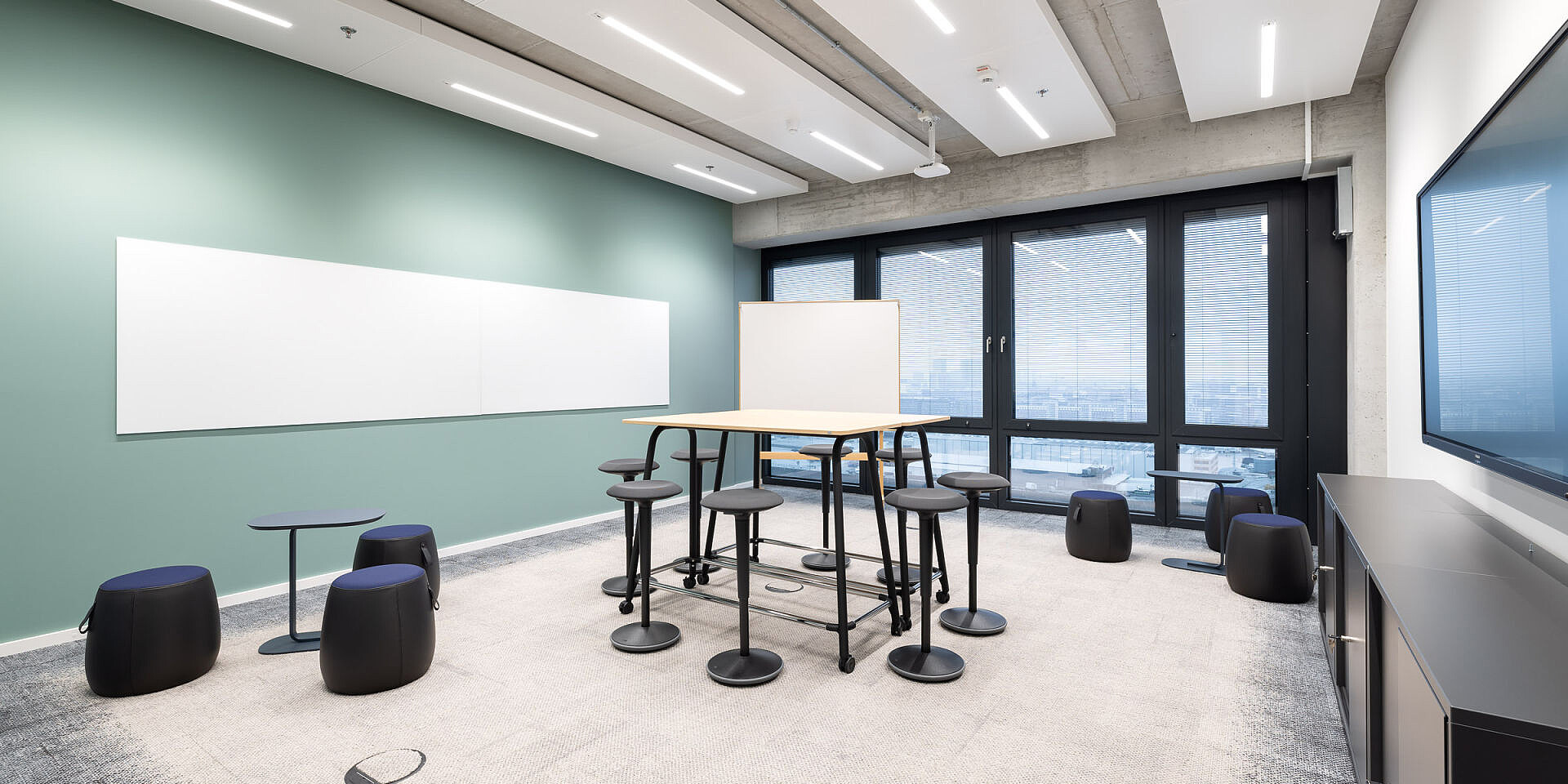 Moderner Meetingraum mit se:lab high desk Workshop-Tisch, se:fit Stehsitzen und se:dot Hockern für agiles Arbeiten und Zusammenarbeit.